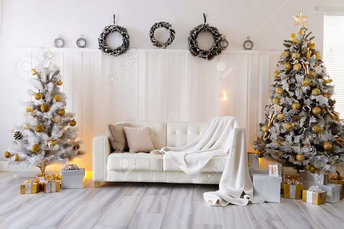 Interno bianco del soggiorno con alberi di Capodanno decorati, scatole regalo e divano moderno. Colore dorato