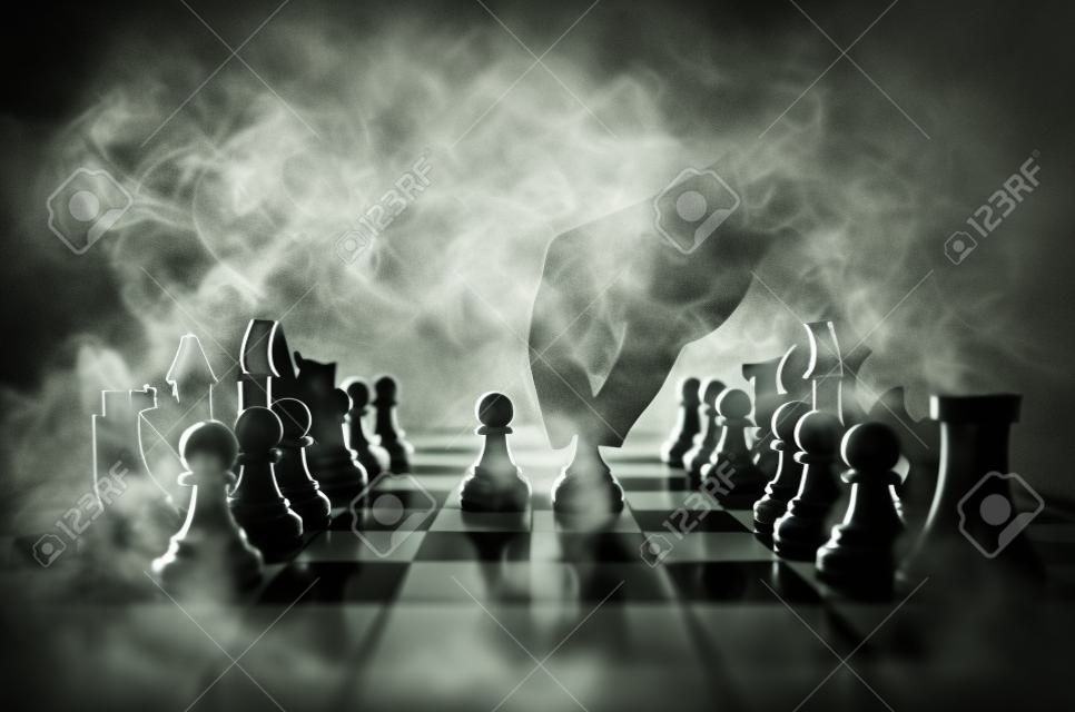 Concepto de juego de tablero de ajedrez de ideas de negocio y concepto de ideas de competencia y estrategia. Figuras de ajedrez sobre un fondo oscuro con humo y niebla. Enfoque selectivo