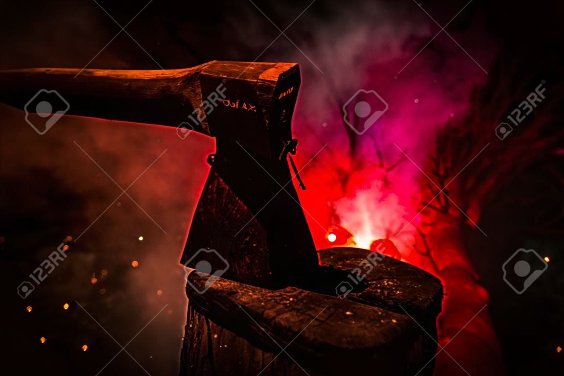 Old ax attached to the tree trunk on horror red foggy background. Scary Halloween theme with maniac killer weapon.