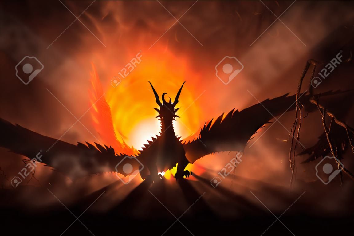 Silhouette of fire breathing dragon with big wings on a dark orange background