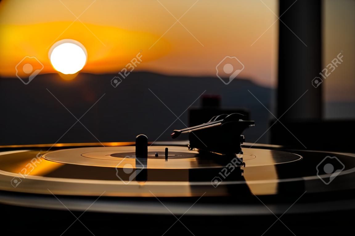 Turntable vinyl record player on the background of a sunset over the mountains. Sound technology for DJ to mix & play music. Black vinyl record. Vintage vinyl record player. Needle on a vinyl record