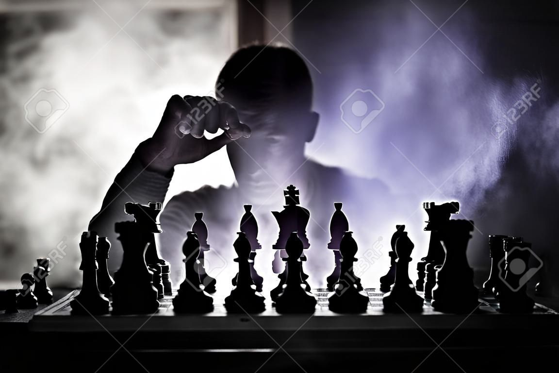 Man playing chess. Scary blurred silhouette of a person at the chessboard with chess figures. Dark toned foggy background. Selective focus. Horror concept