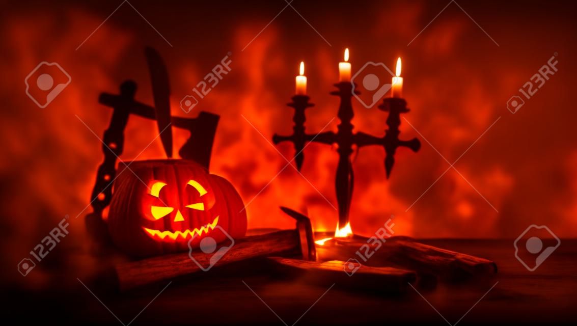 Horror concept. Scary Halloween pumpkin with carved eyes and a smile with burning candles and an ax on a dark toned background. Empty space. Selective focus