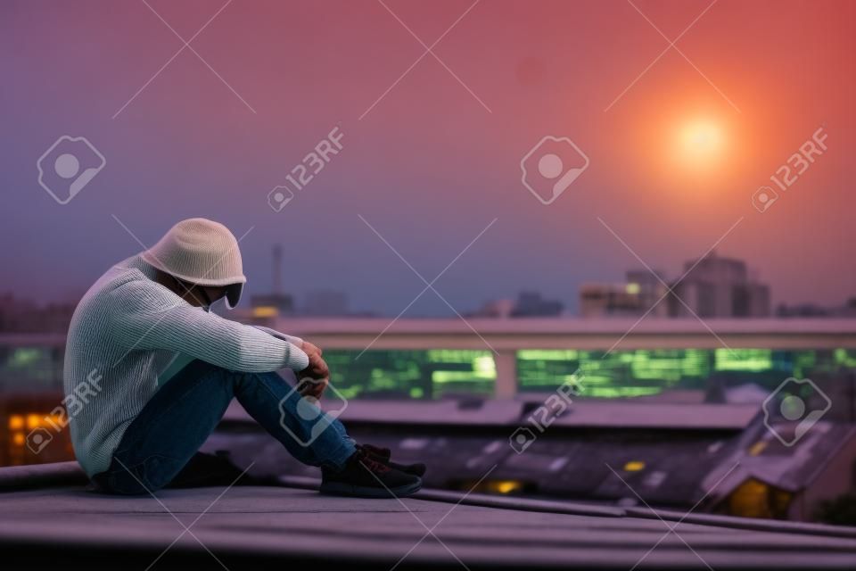 Jonge Aziatische man zittend op het dak van verlaten gebouw met depressie stress uit tijdens zonsondergang tijd in de stad.