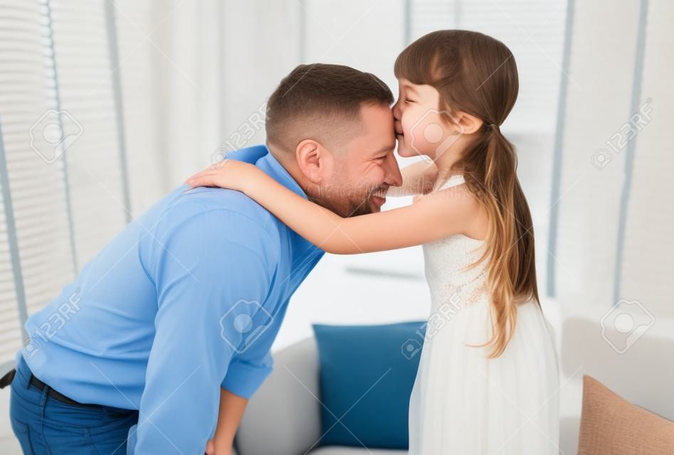 Buona festa della famiglia e del papà. Ritratto di una bambina che bacia suo padre sulla fronte. Amorevole abbraccio bambino e baciare suo padre.