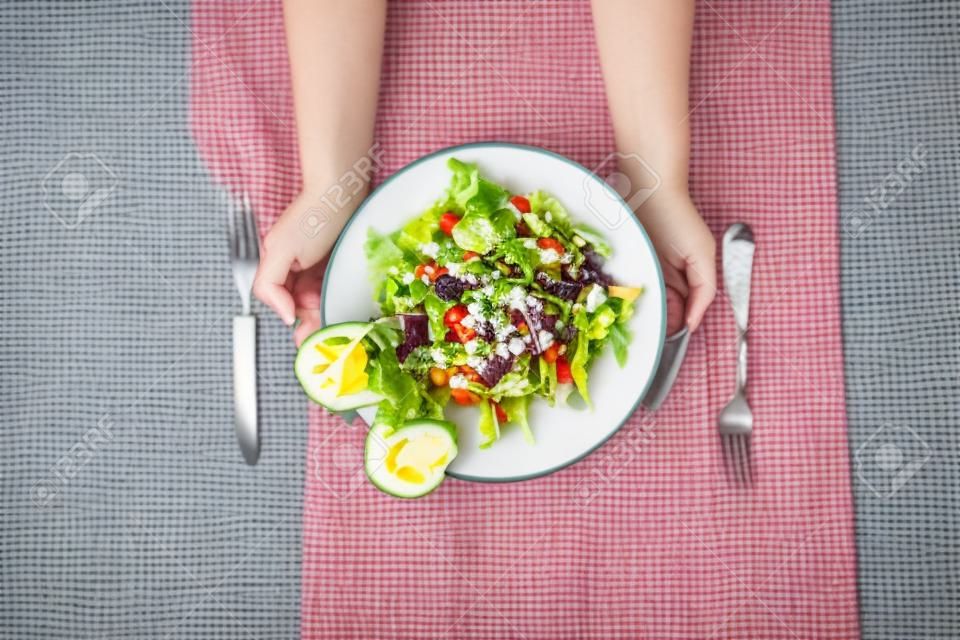 Salade plate avec mains de fille, couteau et fourchette