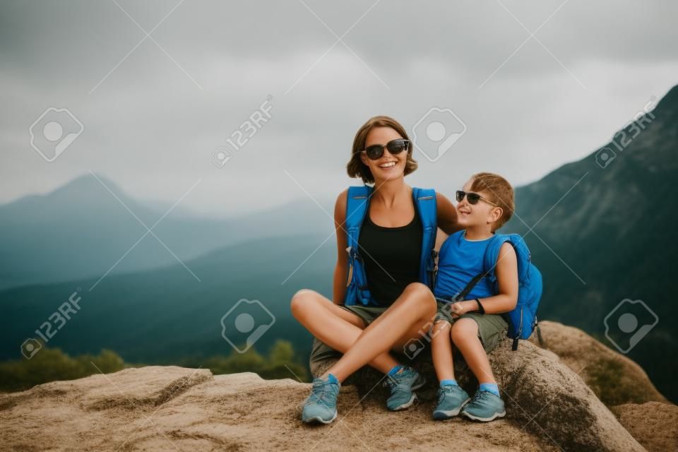 Chłopiec i jego matka siedzą na szczycie góry. Kobieta podróżuje z dzieckiem. Dziecko przytula mamę. Podróżuj z plecakami. Wędruj i wspinaj się z dziećmi. Portret kobiety z synem.