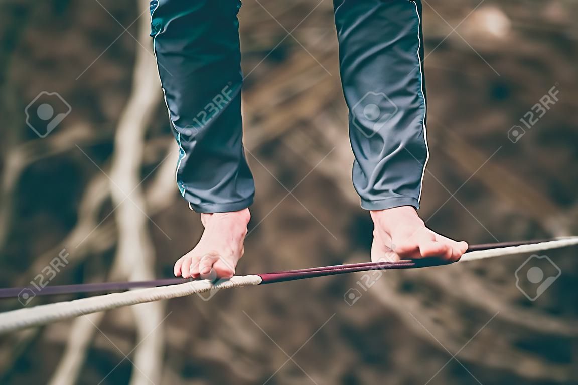 Foot close up. A man is walking along a stretched sling. Highline in the mountains. Man catches balance. Performance of a tightrope walker in nature. Highliner on the background of the mountains.