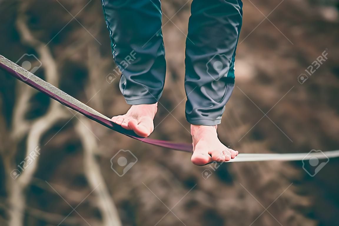 Foot close up. A man is walking along a stretched sling. Highline in the mountains. Man catches balance. Performance of a tightrope walker in nature. Highliner on the background of the mountains.