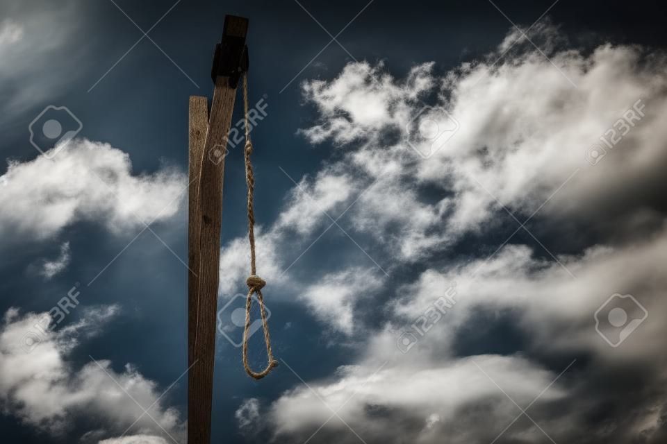 Wooden gallows with old rope and noose against cloudy sky