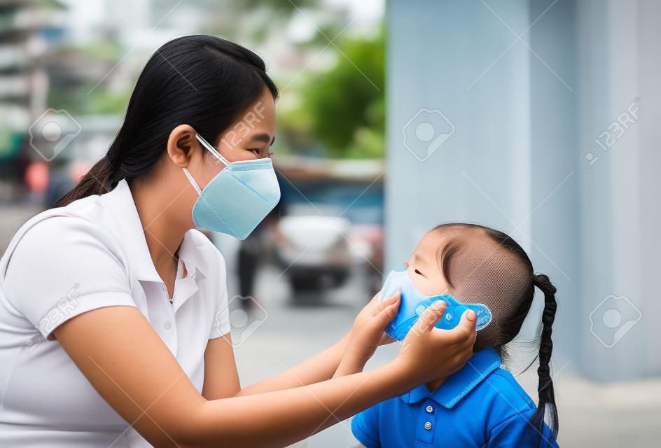 방콕 시에서 PM 2.5 대기 오염에 대비하기 위해 밖에 있는 동안 딸을 위해 보호 마스크를 쓴 아시아계 젊은 어머니. 태국.