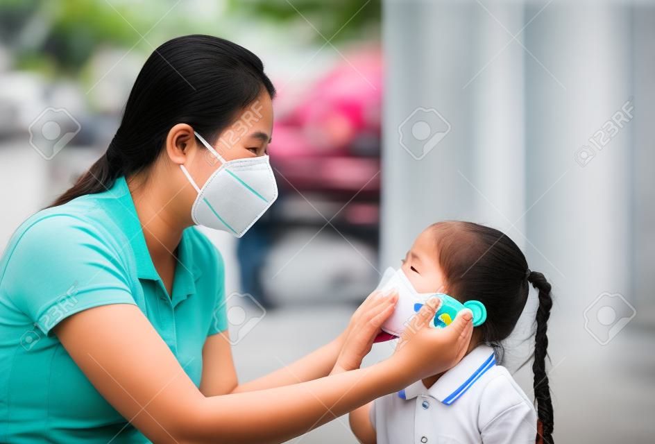 방콕 시에서 PM 2.5 대기 오염에 대비하기 위해 밖에 있는 동안 딸을 위해 보호 마스크를 쓴 아시아계 젊은 어머니. 태국.