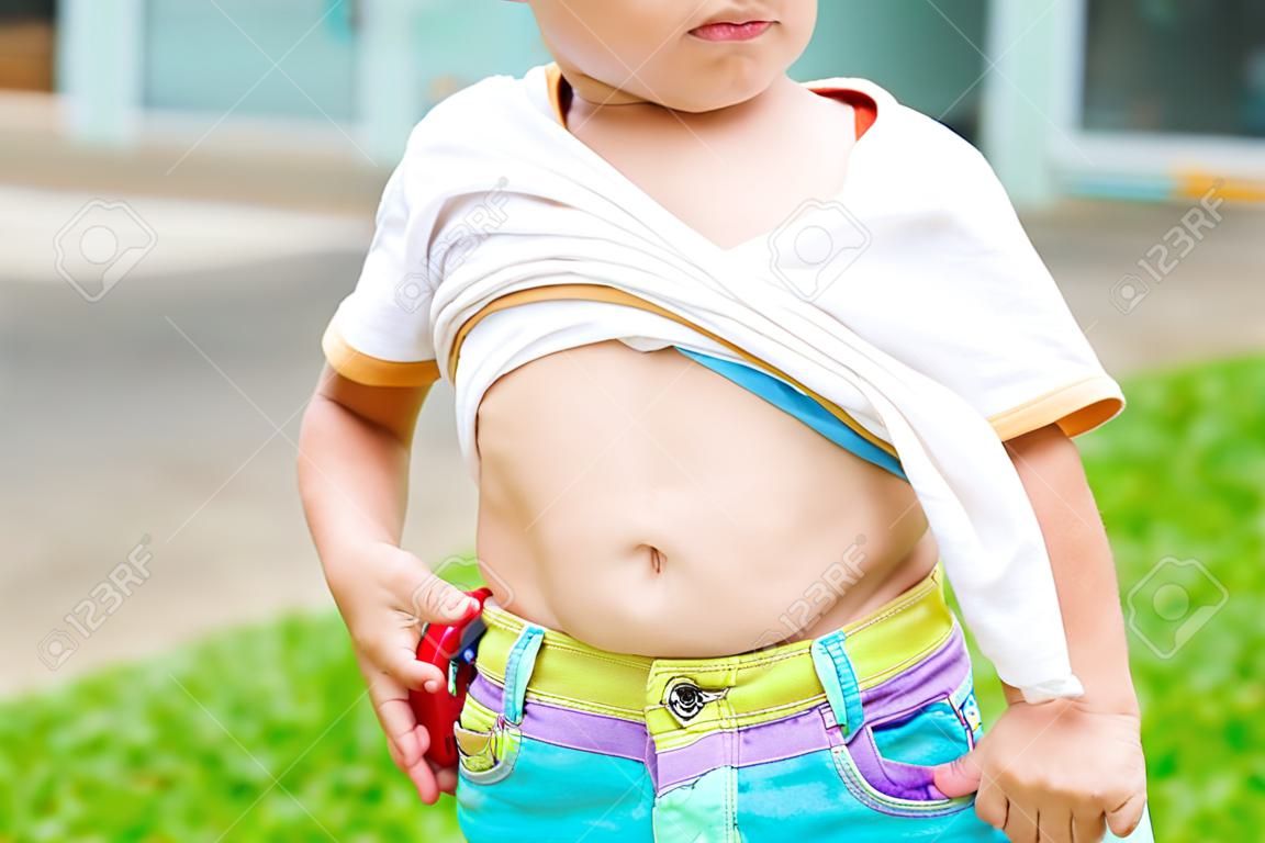 Nahaufnahme kleiner Junge, der sein Hemd anhebt, zeigt seinen großen Bauch.