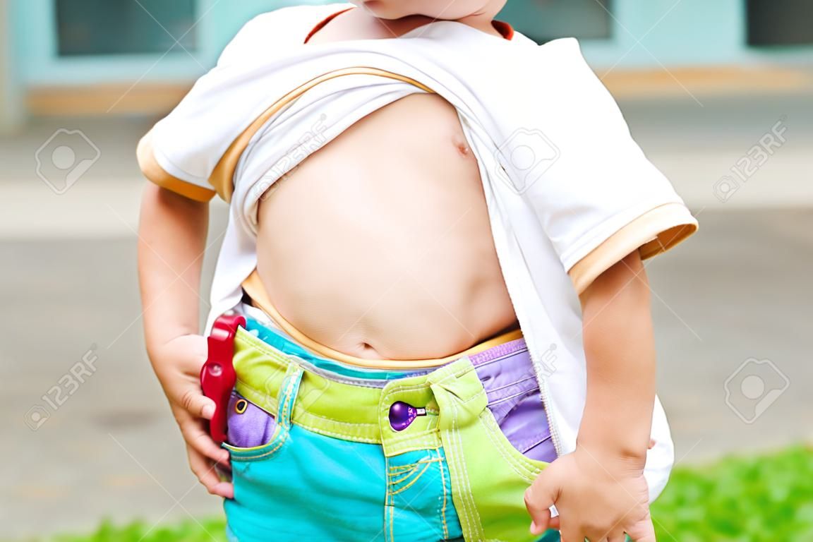 Close up little boy lifting his shirt show exposing his big tummy.
