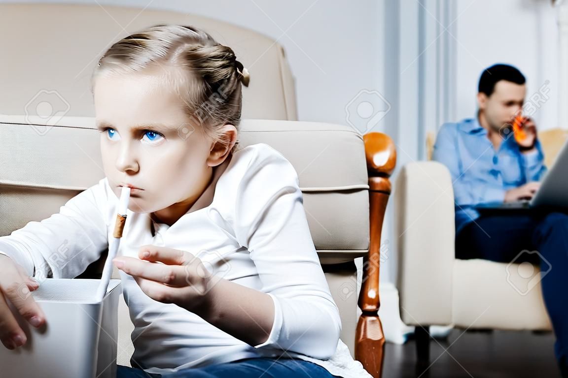 Cigarro. Pobre menina de olhos azuis segurando um cigarro e fumando enquanto seus pais trabalhando em seus laptops