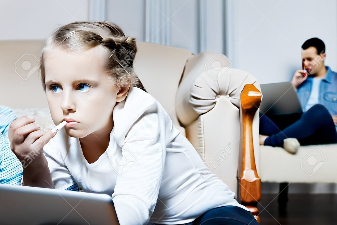 Cigarette. Poor blue-eyed little girl holding a cigarette and smoking while her parents working on their laptops