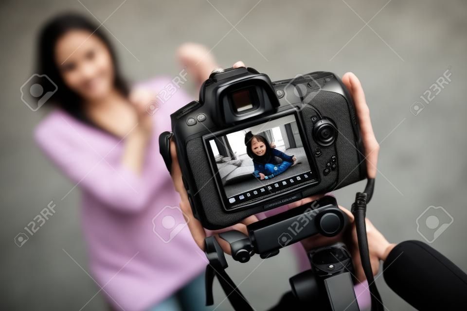 Being a blogger. Black modern digital camera filming a fit slim young woman sitting on the carpet with her laptop and holding a bottle and pointing at it