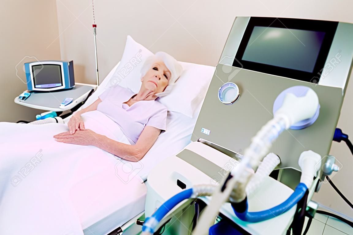 J'aimerais être à la maison en ce moment. Pauvre retraitée concentrant son attention sur un ordinateur alors qu'elle était allongée dans un lit d'hôpital avec un oxymètre de pouls et une assistance respiratoire.