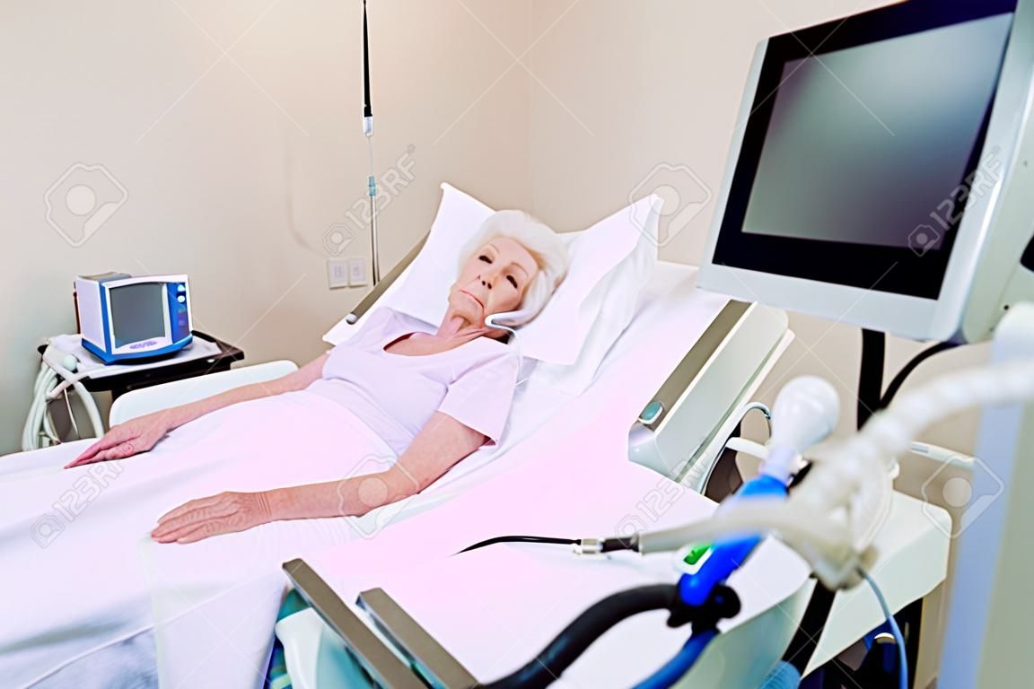 Ich wünschte, ich wäre jetzt zu Hause. Die arme Rentnerin konzentriert ihre Aufmerksamkeit auf einen Computer, während sie mit einem Pulsoximeter und einer Atemhilfe in einem Krankenhausbett liegt.
