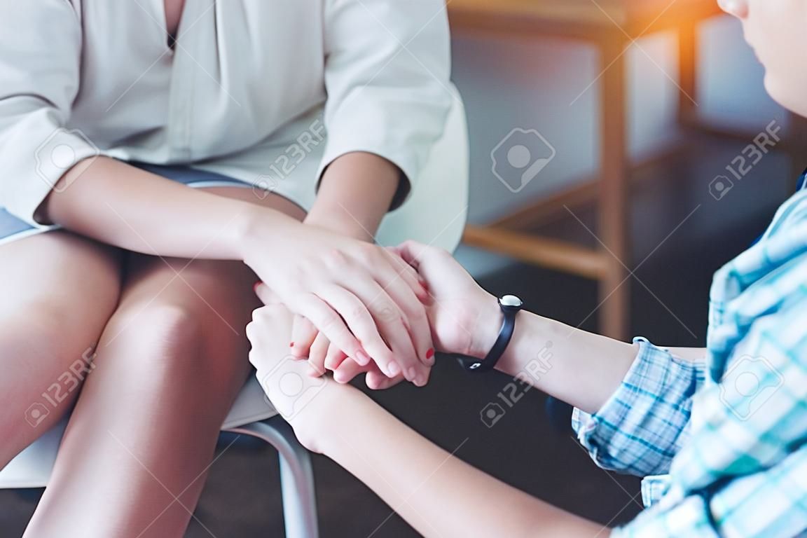 Preciso da tua confiança, perto de um adolescente e de uma psicoterapeuta, de mãos dadas e sentadas à frente uma da outra, durante uma sessão psicológica.