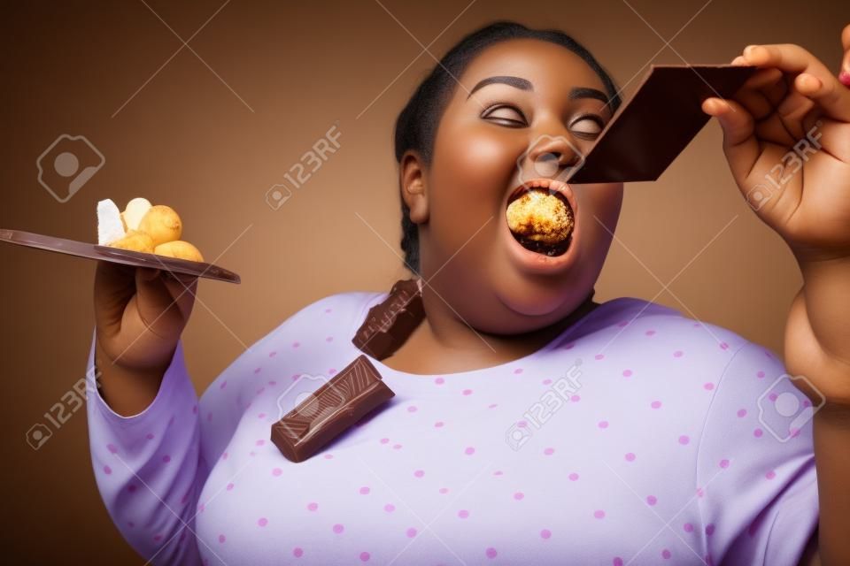 Más chocolate. Mujer joven gordita consumiendo chocolate incontrolablemente