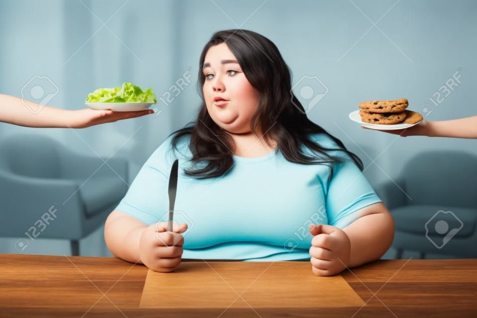 Essere grasso. Miserabile donna grassoccia che guarda un'insalata e che vogliono i biscotti