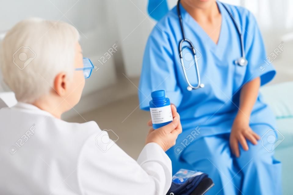 Time for pills. Aged patient with short hair taking pills from caring young nurse in blue uniform