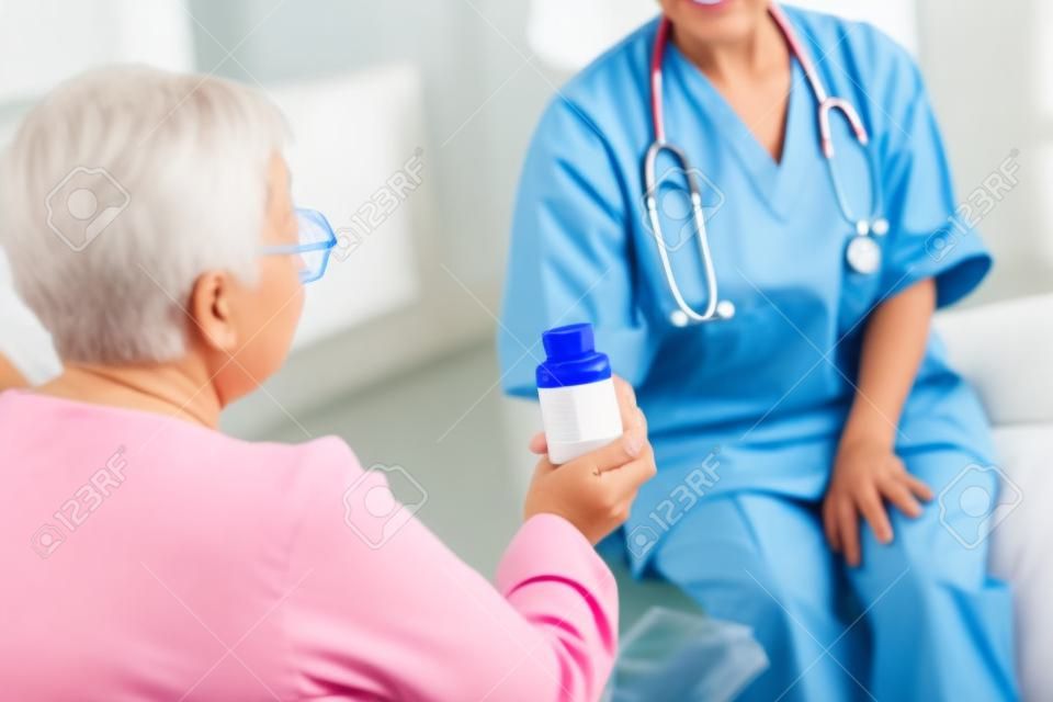 Hora de las pastillas. Paciente anciano con pelo corto tomando pastillas de una joven enfermera cariñosa con uniforme azul