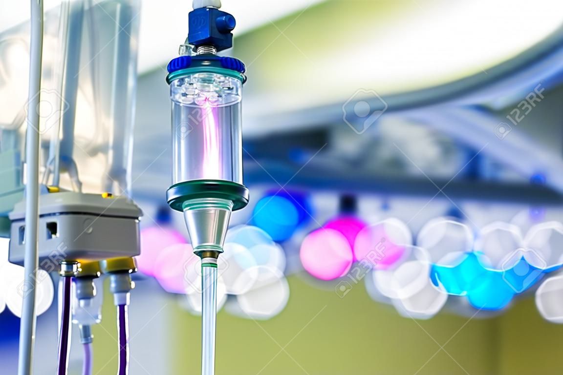Functioning IV drip hanging on a pole in hospital, with LED surgical lights in the background. Patient, illness, treatment, hospital, medicine and healthcare abstract and concept.