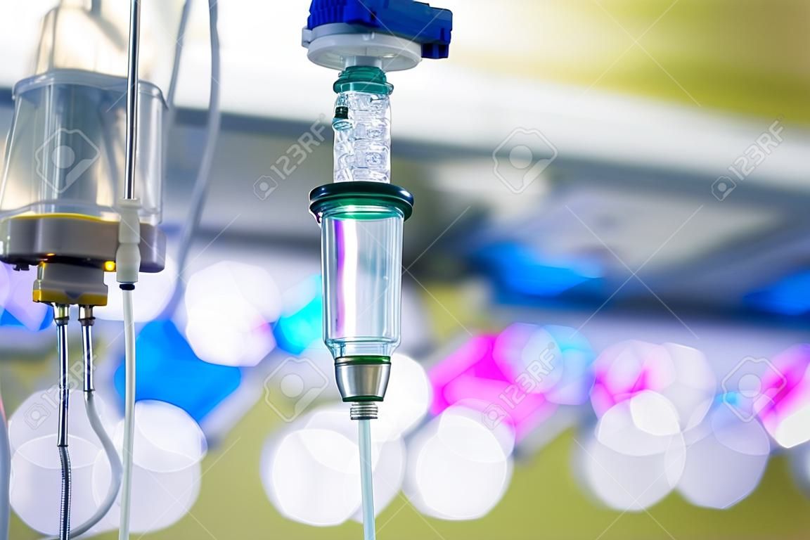 Funzionamento IV flebo appesa a un palo in ospedale, con le luci chirurgiche a LED in background. Paziente, la malattia, il trattamento, ospedale, medicina e della sanità astratto e concetto.
