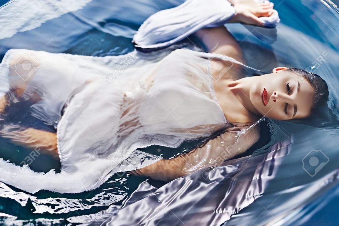 Bliska portret pięknej kobiety leżącej w wodzie z tkaniną. koncepcja mody