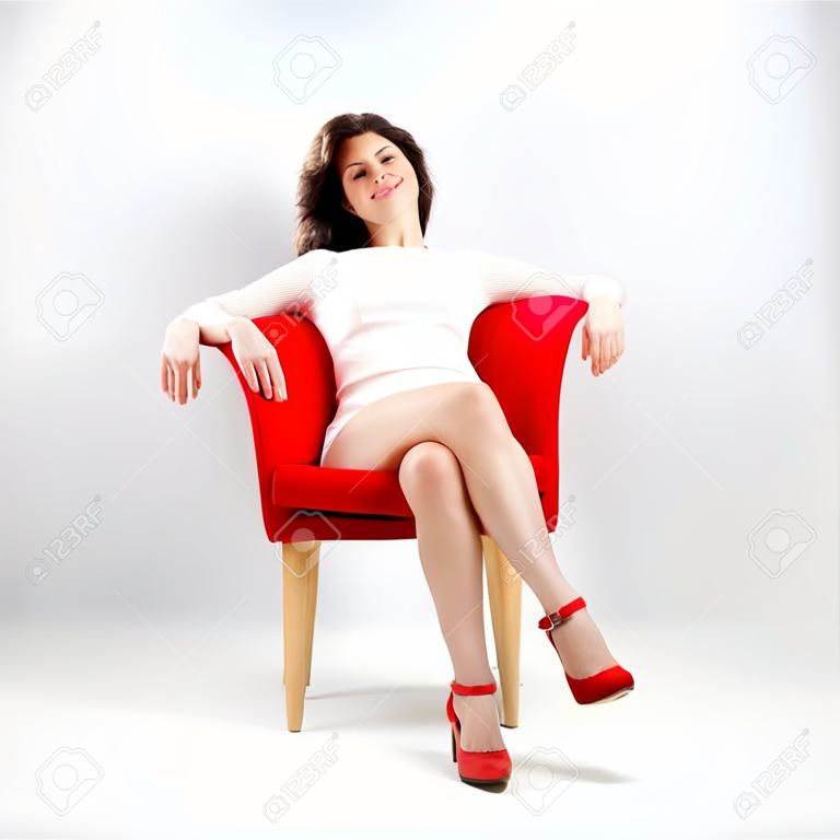 Belle femme souriante détendue sur fauteuil rouge isolé sur gris