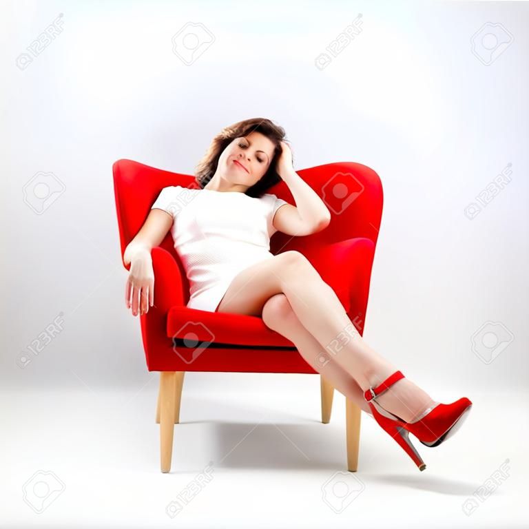 Bella donna sorridente rilassato sulla poltrona rossa isolato su grigio