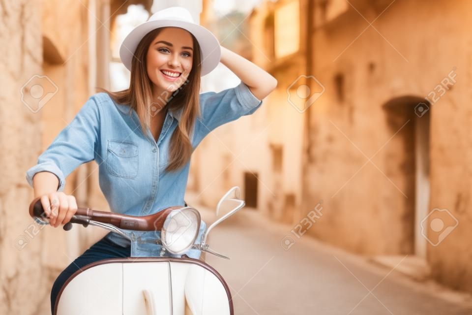 beautiful girl in a hat in a white t-shirt and hat posing on a vintage scooter in Italy fashion clothing and accessories bracelet on her arm