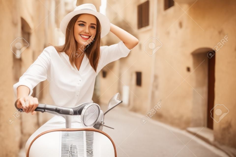 Schöne Mädchen in einem Hut in einem weißen T-Shirt und Hut posiert auf einem Vintage Roller in Italien Mode Kleidung und Zubehör Armband auf dem Arm