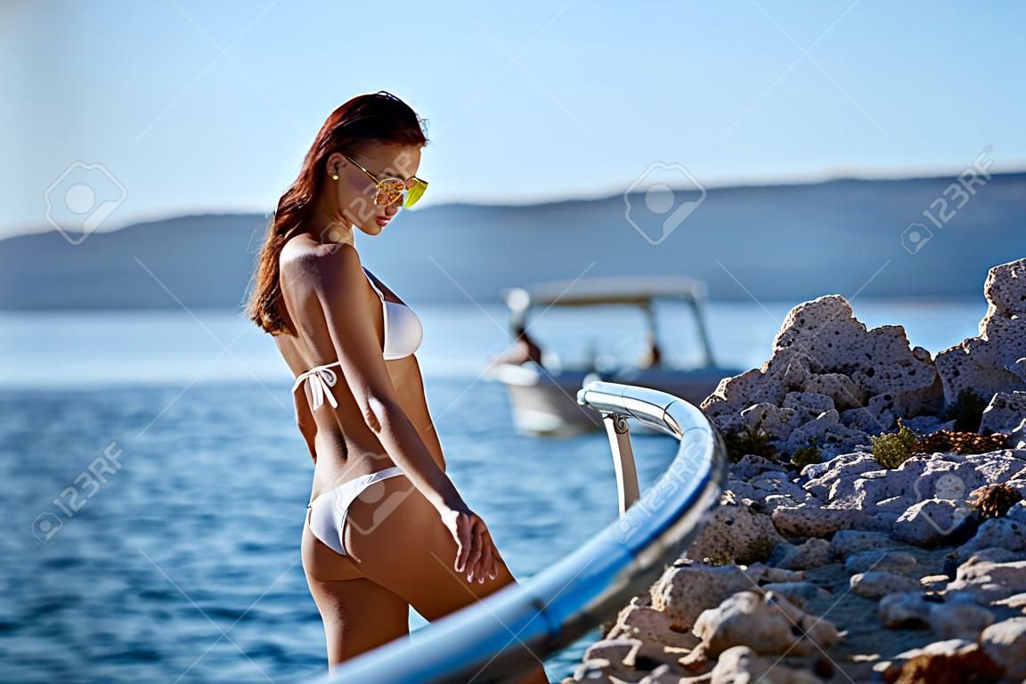 girl with a beautiful body sunbathes on a beach in a white bathing suit against the sea