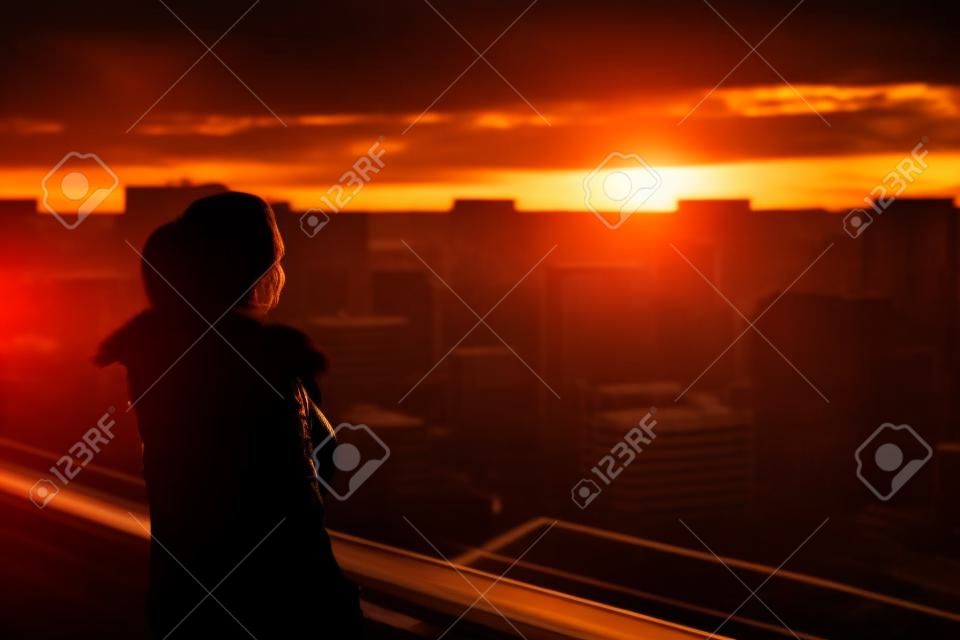 Silhouette of woman enjoying the city view on sunset. Concept of loneliness, eternity, choice