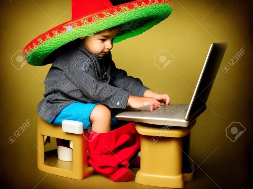 Ragazzo carino con cappello messicano sulla testa, seduta sulla toilette con il portatile
