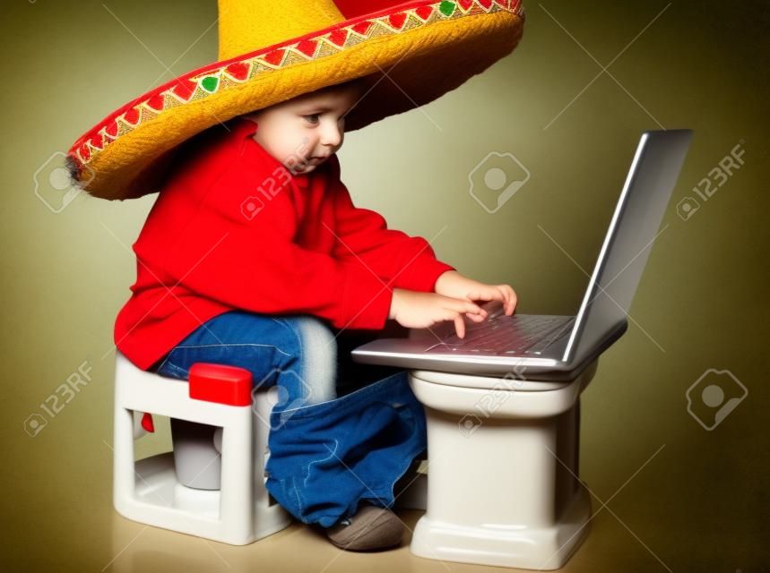 Ragazzo carino con cappello messicano sulla testa, seduta sulla toilette con il portatile