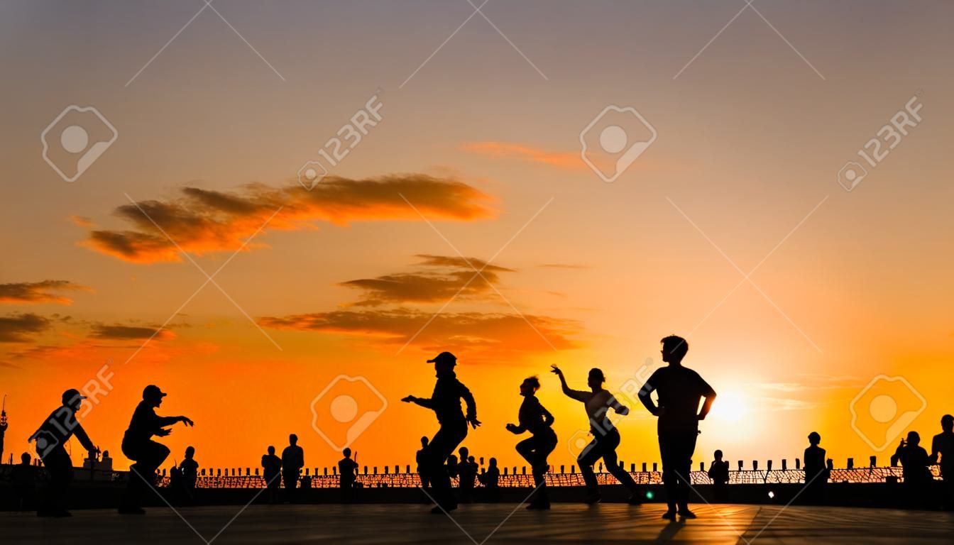 Silhouette di persone irriconoscibili che imparano a ballare - sull'argine della città al tramonto. Street dance, formazione, insegnamento, istruzione, istruzione, estate e concetto di cultura urbana