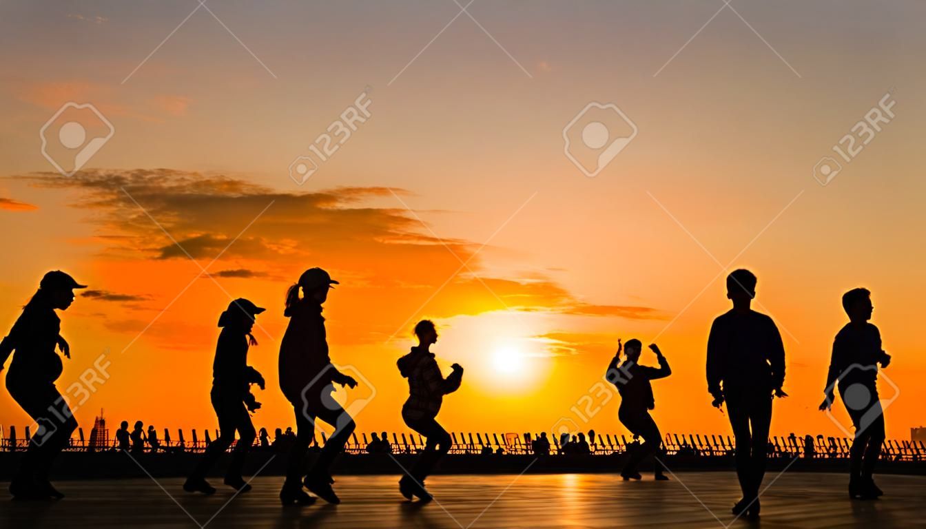 Silhouette di persone irriconoscibili che imparano a ballare - sull'argine della città al tramonto. Street dance, formazione, insegnamento, istruzione, istruzione, estate e concetto di cultura urbana