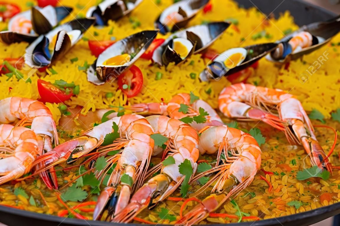 Close up: cooked yellow paella with shrimp, mussel, rice, spice, saffron in huge paella pan at summer outdoor food market. Spanish cuisine, seafood, gastronomy, street food concept