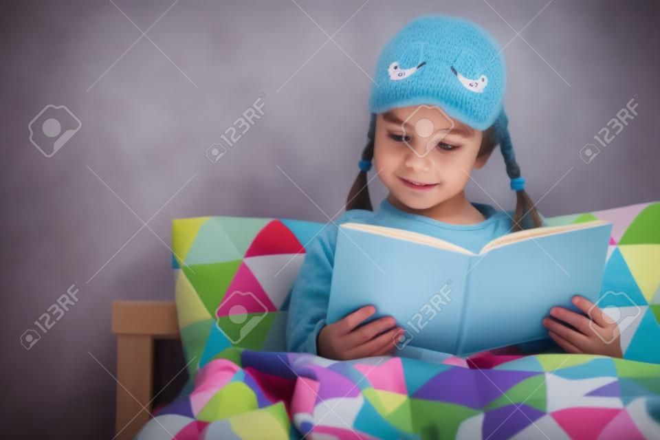 Pilna dziewczynka czyta w łóżku w piżamie przed pójściem spać na niebiesko