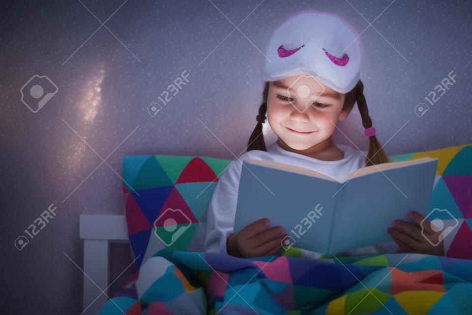 Pilna dziewczynka czyta w łóżku w piżamie przed pójściem spać na niebiesko