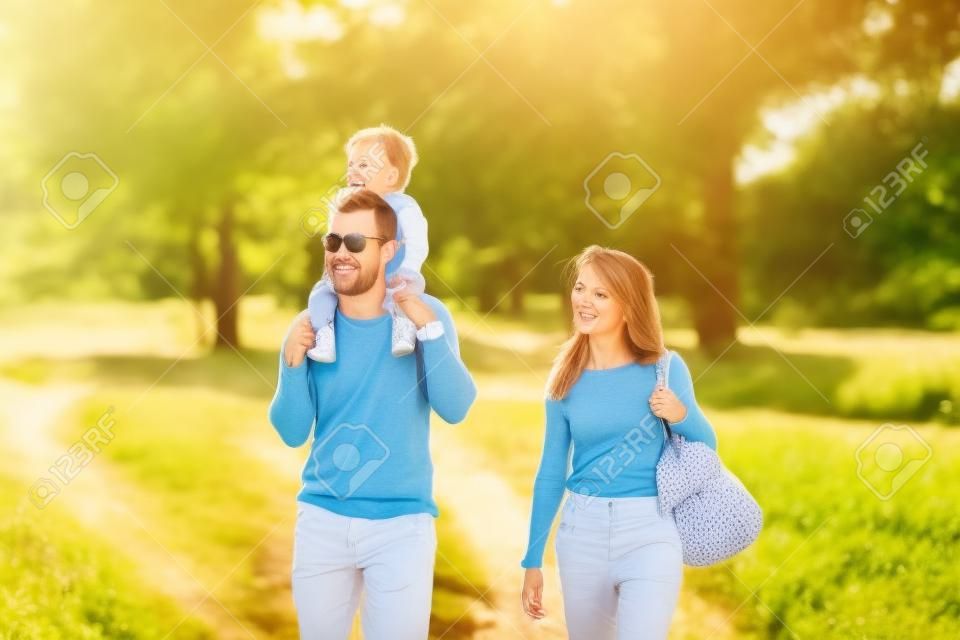 Famiglia idilliaca felice che cammina in campagna durante la bella giornata di sole all'esterno. Babby cavalca sulle spalle di suo padre, lui e sua moglie non riescono a smettere di sorridere.